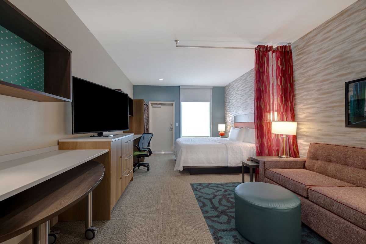 Een hotelkamer met een bed, een bureau met stoel, een televisie, een bank en een lamp.