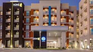 Een modern hotel met meerdere balkons, een centrale ingang en een opvallend 'HOME 2 by Hilton'-bord.