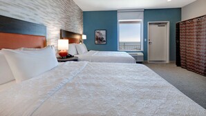 Hotelkamer met twee bedden, een nachtkastje met lamp, een raam met uitzicht en een deur.