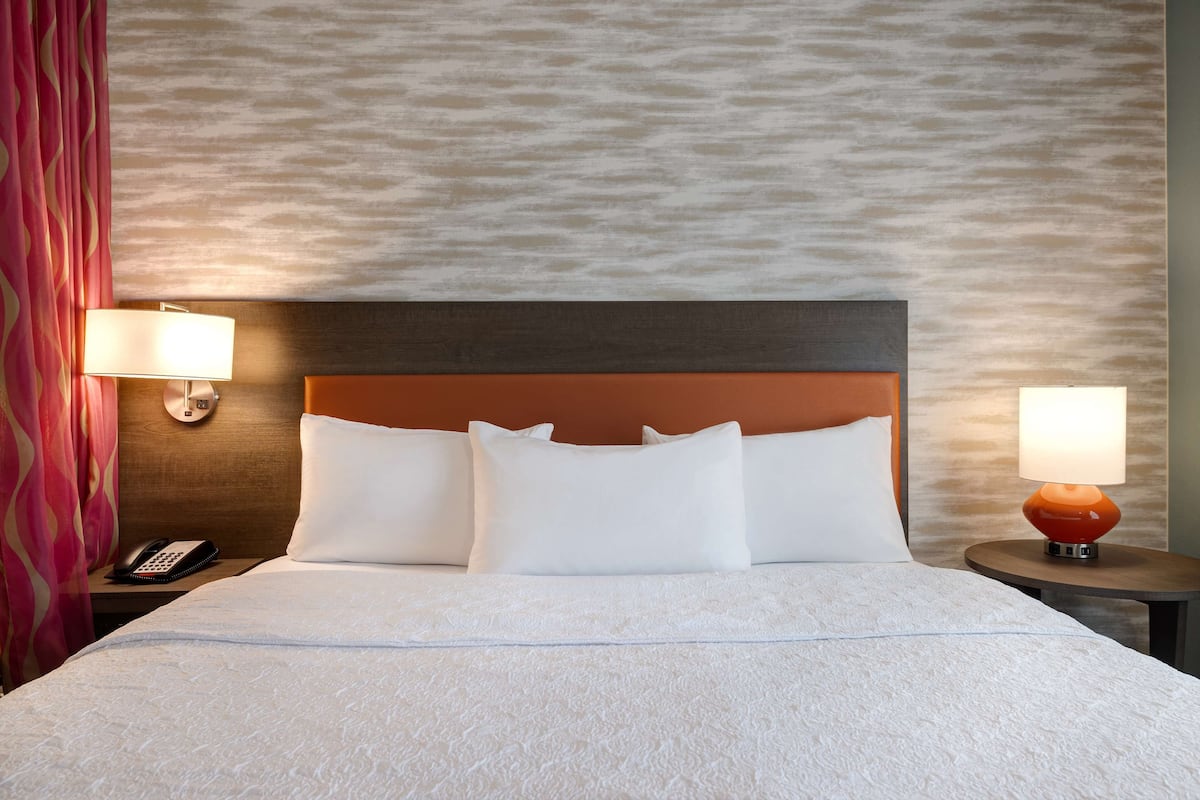 Een hotelkamer met een bed, twee bedlampen, een telefoon en een behang met patroon.