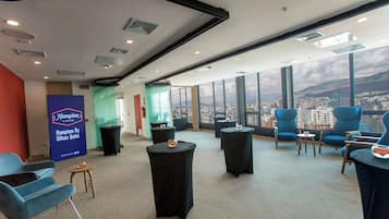 A modern hotel room with a city view, comfortable seating, and a Hampton By Hilton sign.