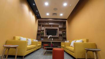 Un salon moderne avec des canapés jaunes, un pouf rouge et un téléviseur à écran plat fixé au mur.