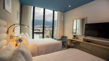 Une chambre d’hôtel avec deux lits, un bureau avec une chaise, une télévision et une grande fenêtre donnant sur la ville.