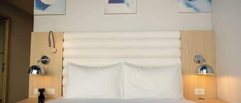 Una habitación de hotel con una cama grande, dos mesitas de noche, una lámpara de pared y arte abstracto sobre la cama.