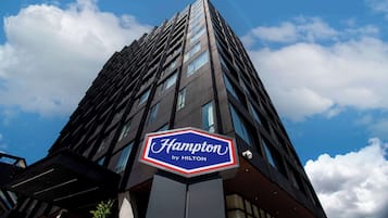 A hotel sign with the name "Hampton by Hilton" against a clear sky.