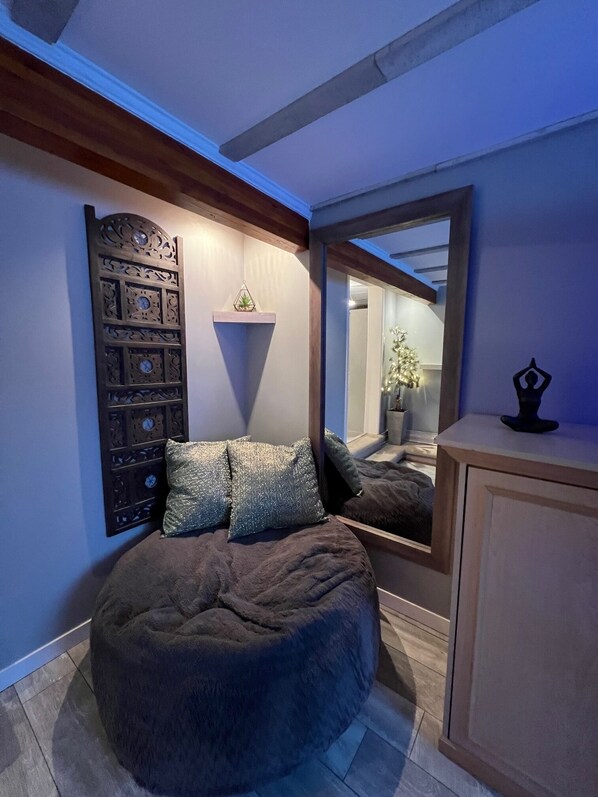 A cozy room with a round bean bag chair, a decorative wall panel, a small shelf with a plant, and a mirror reflecting a staircase. - Mt. Washington Ski Chalet in the Alpine Village (Courtenay)