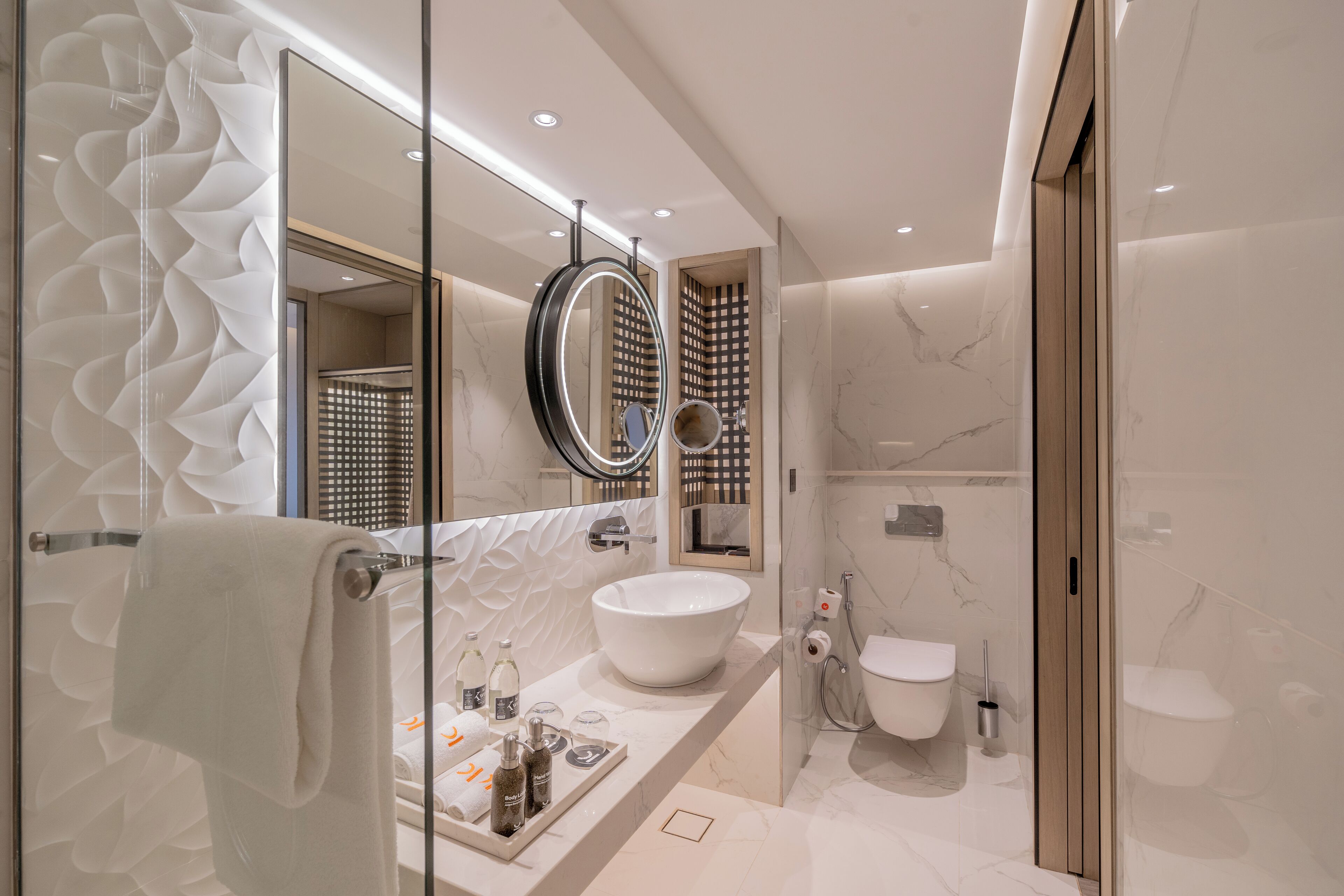 A modern bathroom with a large white sink, a round mirror, and a glass shower enclosure.