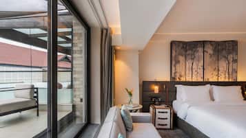 Habitación de hotel moderna con una cama grande, un sofá, una mesita con una lámpara y vistas al balcón exterior.