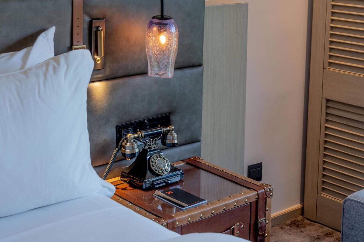 Una habitación de hotel con una cama, un teléfono antiguo y una lámpara colgante original.
