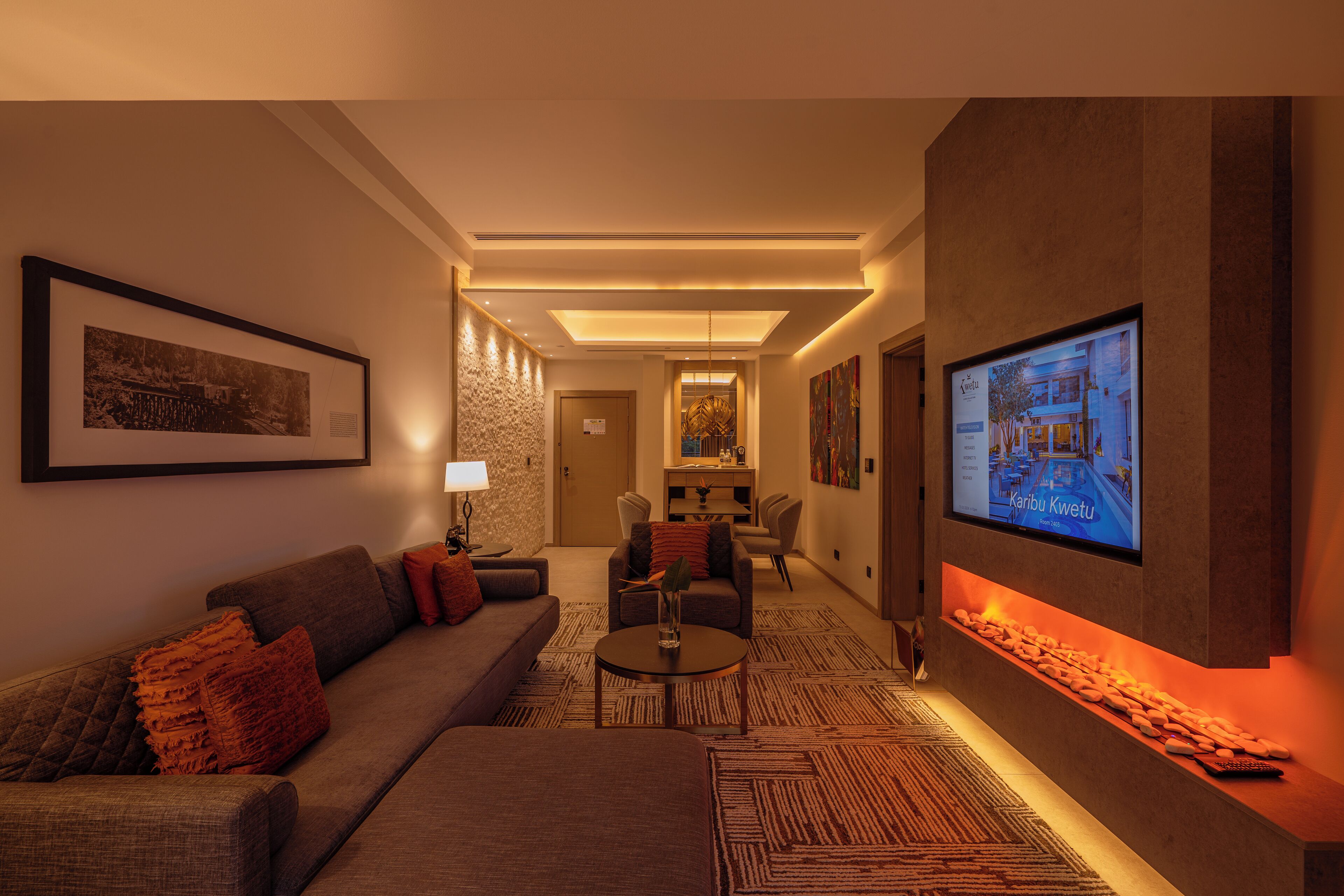 Un hall d’hôtel moderne avec un canapé, des fauteuils, une table basse, une cheminée et un écran de télévision.