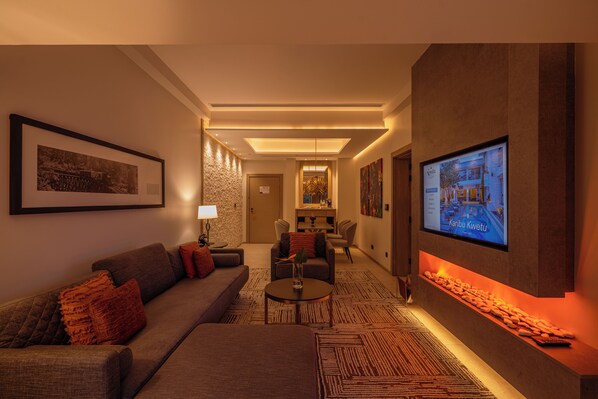 Rebedor modern d'un hotel amb un sofà, butaques, una taula de cafè, una llar de foc i una pantalla de televisió.