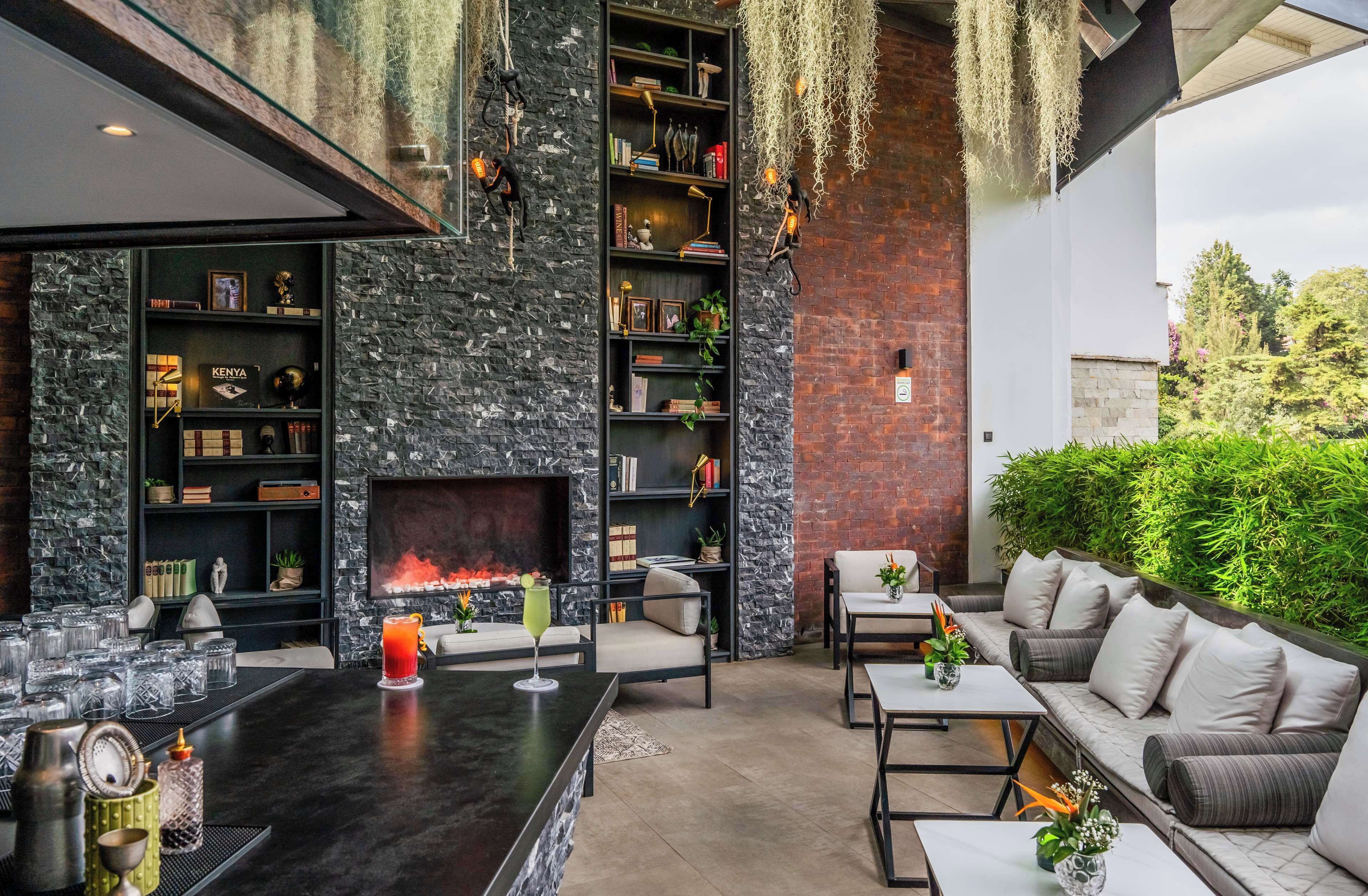 Een moderne buitenlounge met een stenen muur, boekenkasten, een open haard, zitplaatsen en een bar.