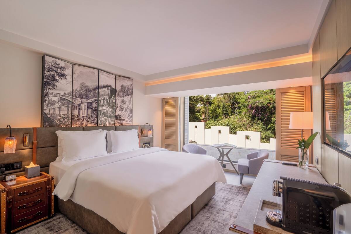 Habitación de hotel moderna con una cama grande, un escritorio con lámpara, una mesita y vistas al exterior.