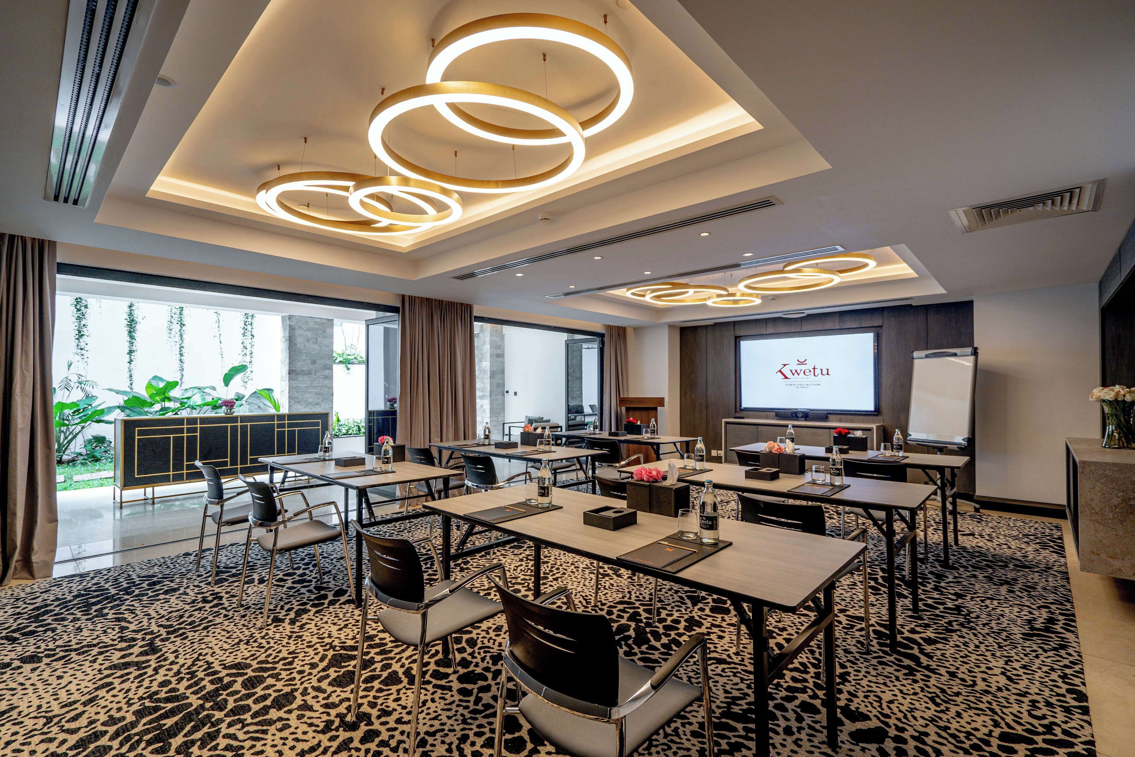 Une salle de conférence moderne avec un tapis à motifs léopard, des tables rondes et un grand écran affichant le mot « Kwetu ».