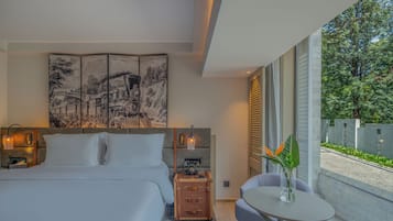 Quarto de hotel moderno com uma cama grande, um quadro na parede, uma pequena mesa com um vaso e vista para o exterior.