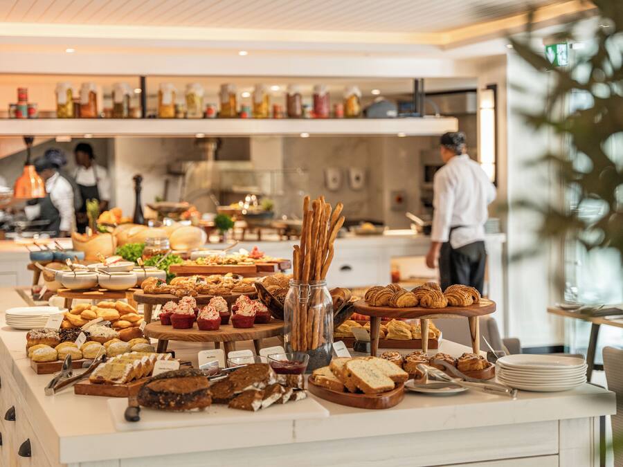 A buffet with various food items and a kitchen area in the background.