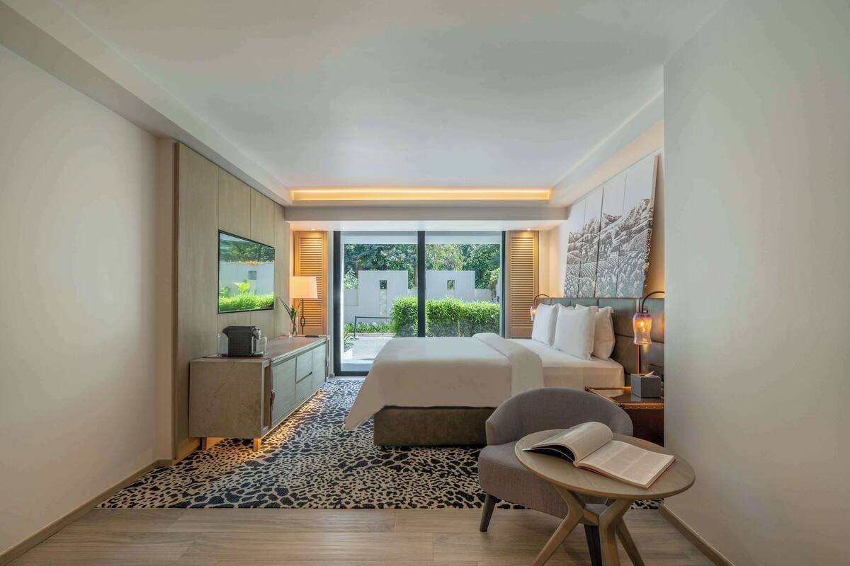 Habitación de hotel moderna con cama, escritorio, silla, una mesita y vistas al exterior.
