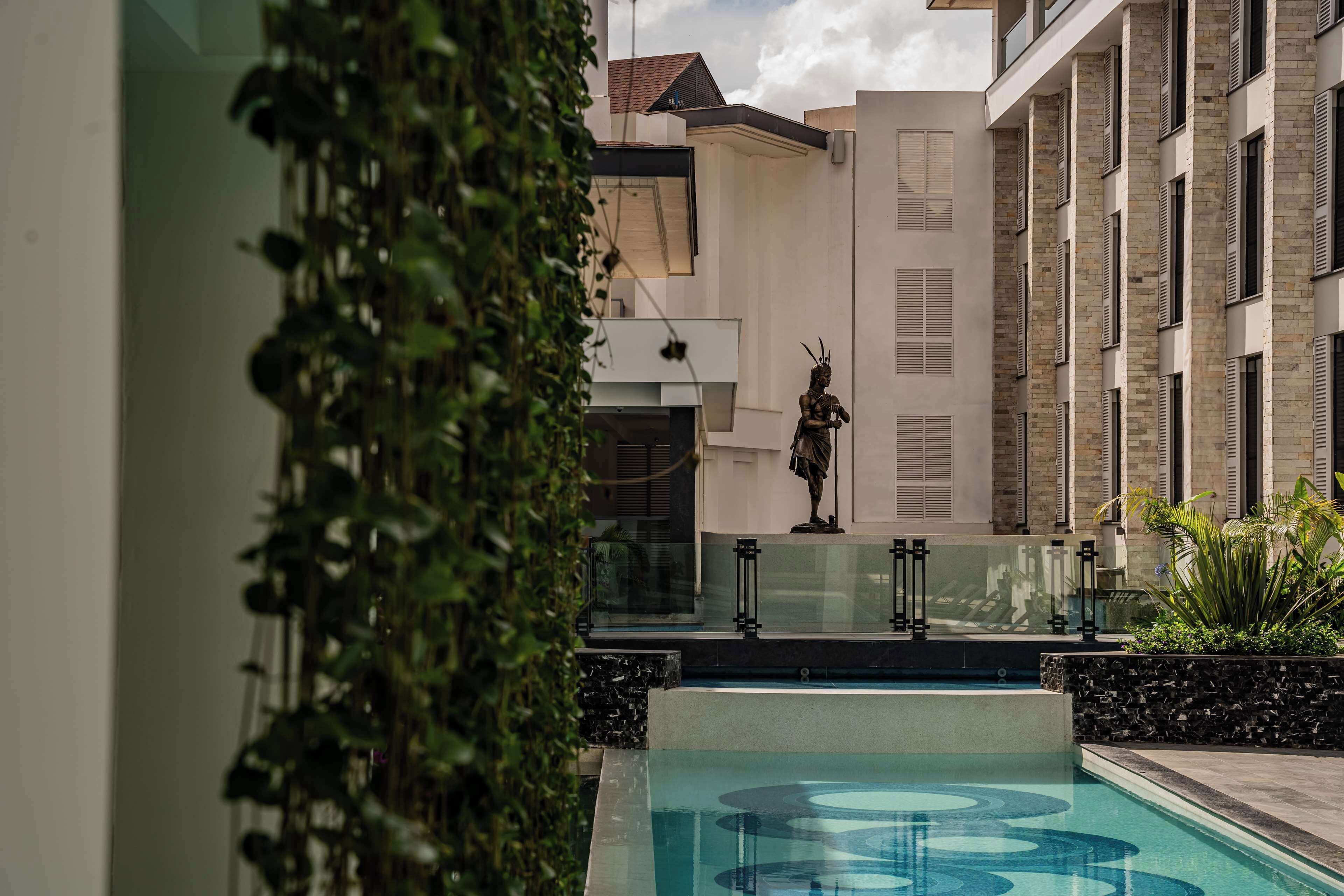 A modern building with a pool, a statue, and greenery.