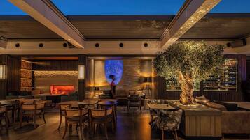 A modern lounge area with seating arrangements, a fireplace, and a large tree.