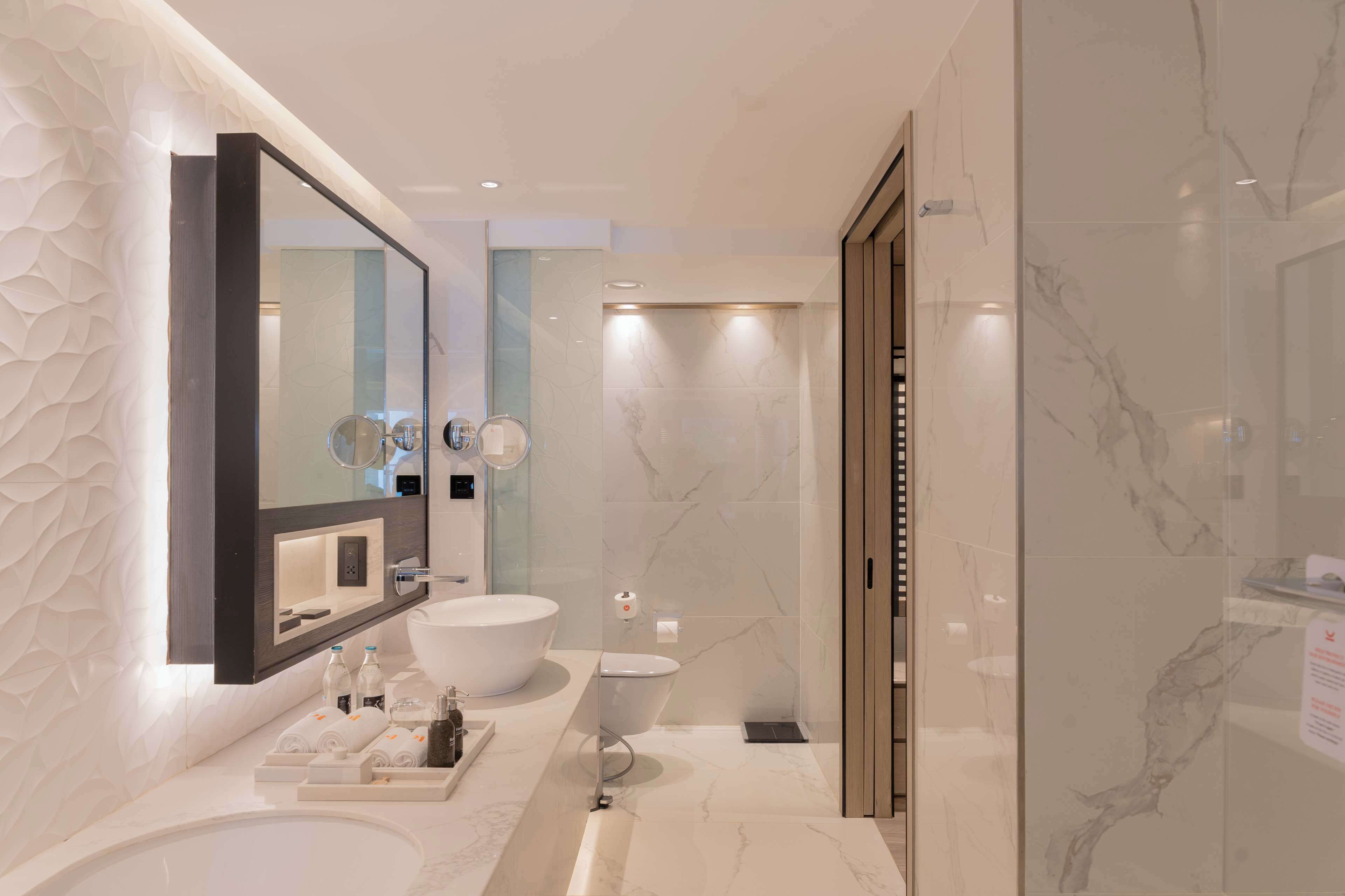 A modern bathroom with a large mirror, two sinks, a bathtub, and a shower.