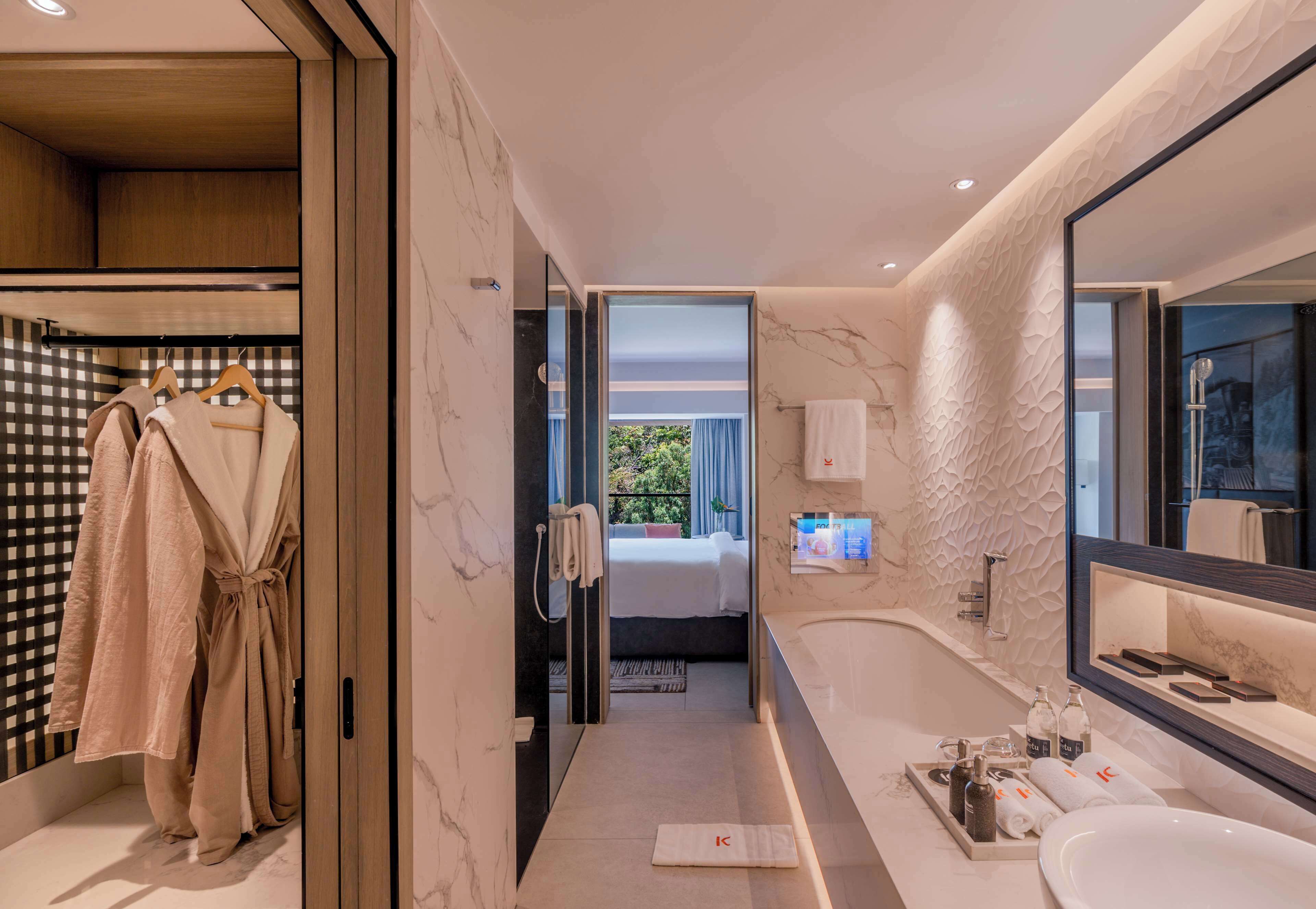 A modern bathroom with a large mirror, a bathtub, and a shower. There is a robe rack with robes hanging on it.