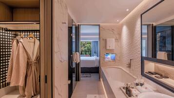 Un baño moderno con un espejo grande, una bañera y una ducha. Se ve un perchero con batas colgadas.