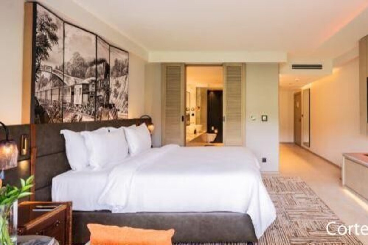 A modern hotel room with a large bed, a flat-screen TV, a sofa, and a dining area.