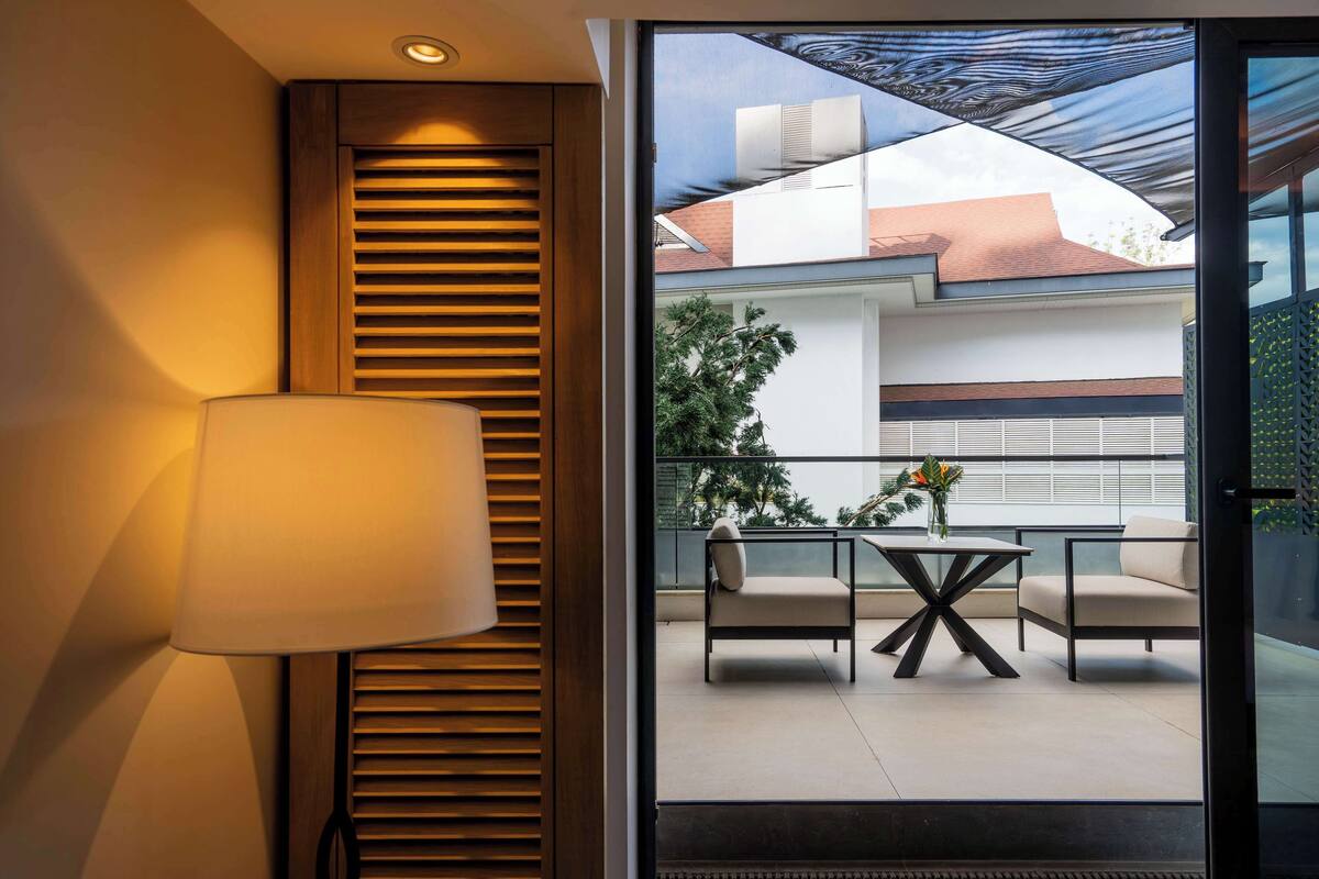Una habitación moderna con un gran ventanal, una lámpara de pared y vistas a un área de estar exterior con una mesa y sillas.