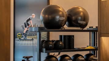 A home gym with a stationary bike, two large exercise balls, and various weights on shelves.