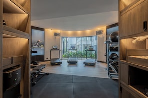 A modern gym with treadmills, exercise equipment, and large windows offering a view of buildings outside.