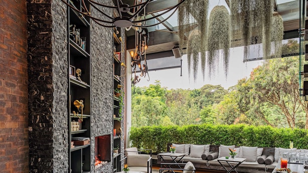 A modern interior with a stone wall, a fireplace, and a seating area with a view of lush greenery. - Kwetu Nairobi, Curio Collection By Hilton (Nairobi)