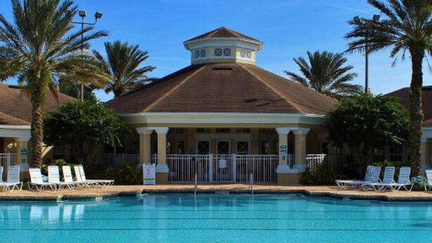 A hotel with a swimming pool, palm trees, and a covered area with lounge chairs.