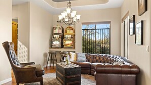 Un salon avec un canapé en cuir, un fauteuil à capitons, une table basse et un lustre.
