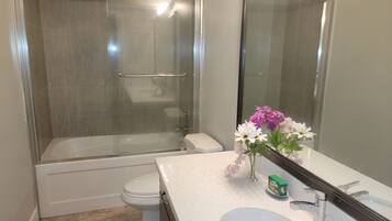Un baño con ducha envuelta en cristal, inodoro y lavabo con espejo.