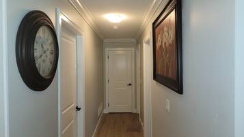 Un couloir avec une horloge, une porte et un tableau encadré accroché au mur.