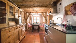 Een landelijke keuken met houten kastjes, een eettafel met stoelen en een moderne kookplaat.