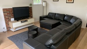 A modern living room with a sectional sofa, a flat-screen TV, a white cabinet, and a brick wall. - Amazing location across the road from Mount Martha South Beach Check in 10am (Mount Martha)