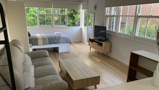 A modern, open-plan living space with a bed, sofa, TV, and wooden flooring. - Amazing location across the road from Mount Martha South Beach Check in 10am (Mount Martha)