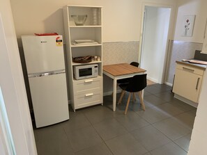 Et kompakt køkken med køleskab, mikroovn og et lille spisebord med en stol.