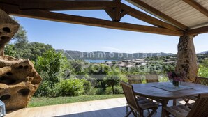 Une terrasse en bois avec une table et des chaises, offrant une vue panoramique sur un paysage pittoresque composé de collines et d’une étendue d’eau.