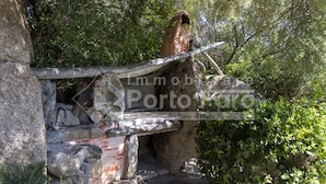 Un pont de pierre rustique, surmonté d’une passerelle en bois, enjambe un terrain rocheux et est entouré d’une végétation luxuriante.