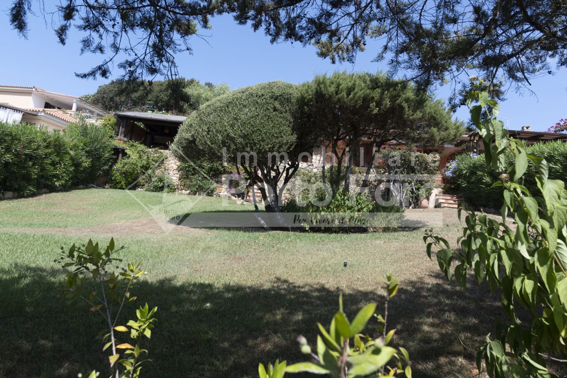 Un jardin bien entretenu, agrémenté de divers arbres et arbustes, d’une zone dallée et d’un mur en pierre.