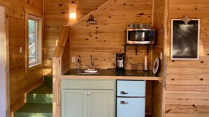 A compact kitchen with wooden walls, a microwave, a sink, and a small refrigerator. - Coach's Quarters - The Dugout - Come Spend The Night in the Trees!! (Waco)
