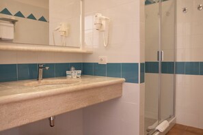 A bathroom with a sink, mirror, hairdryer, and a glass-enclosed shower.