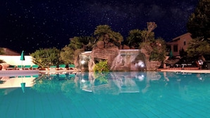 A swimming pool with a waterfall feature, surrounded by palm trees and a night sky with stars. - Le Residenze Del Golfo Di Orosei Bilo 5 (Orosei)