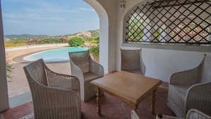 A covered patio with wicker furniture, a pool, and a view of the landscape. - Il Giardino Degli Oleandri Bilo 4 (Arzachena)