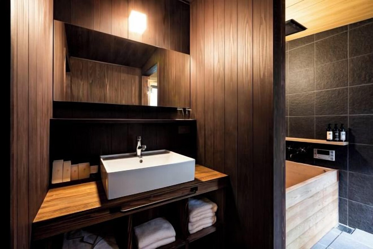 A modern bathroom with a wooden vanity, a large mirror, and a dark tiled shower area.
