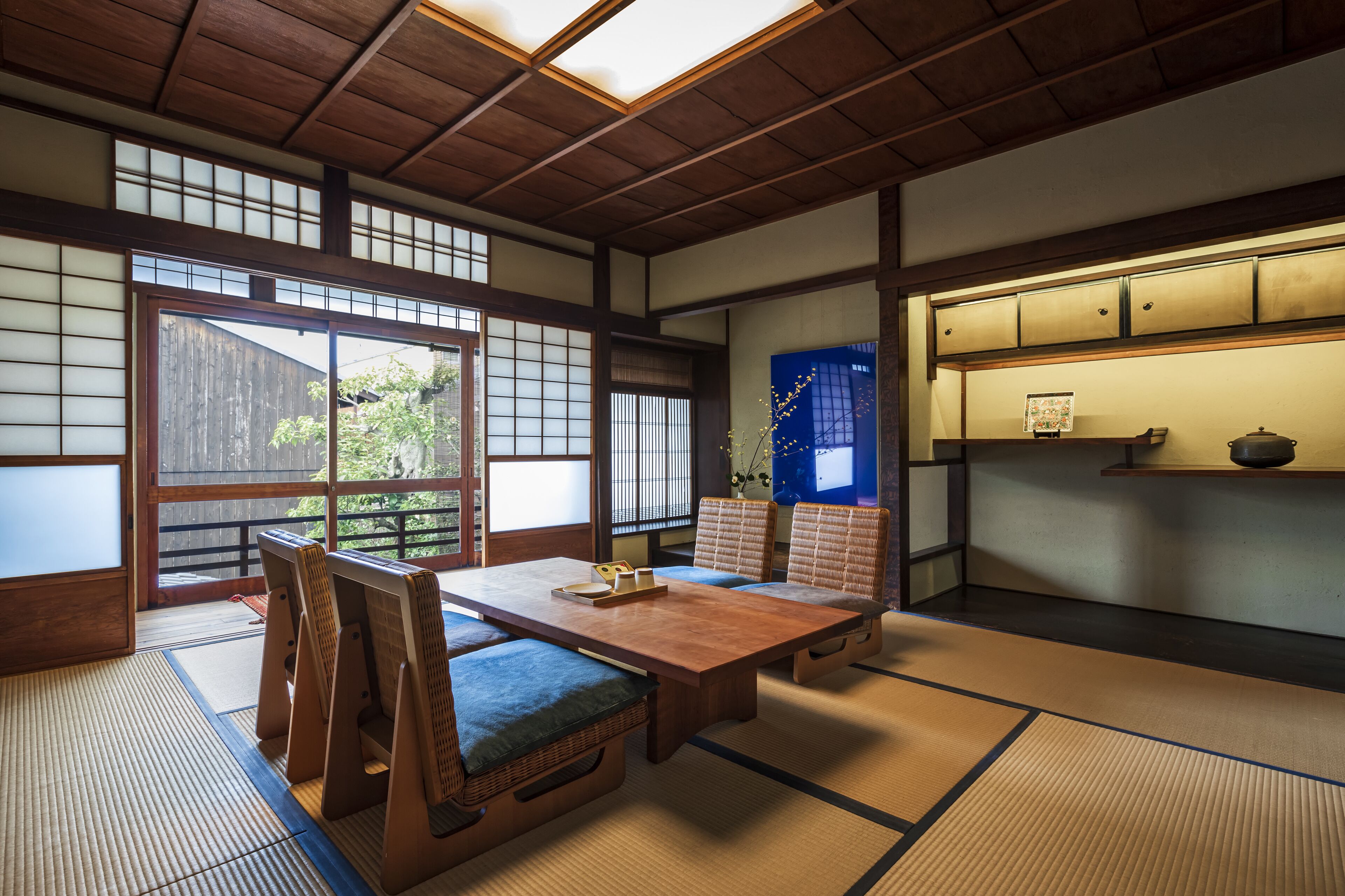 A traditional Japanese room with tatami flooring, a low wooden table, and a sliding door leading to an outdoor area.