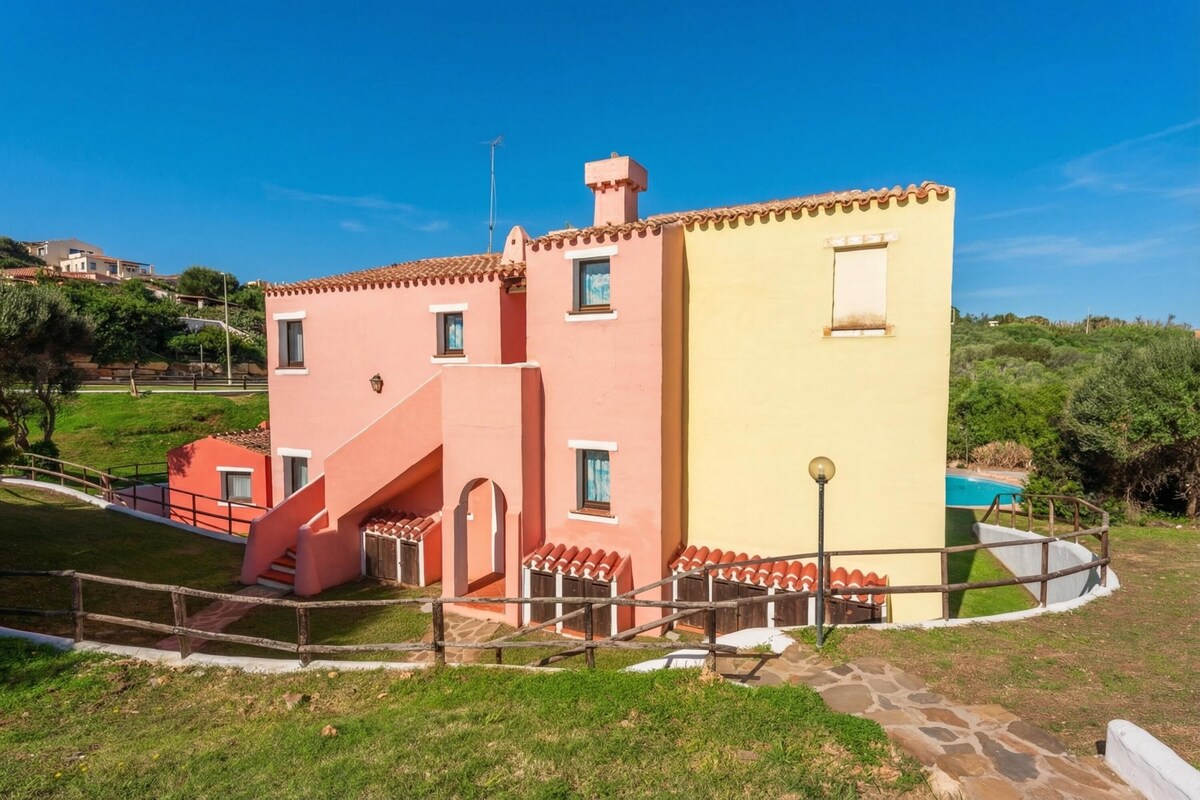 A two-story building with a red and yellow facade, a staircase, and a pool in the background.