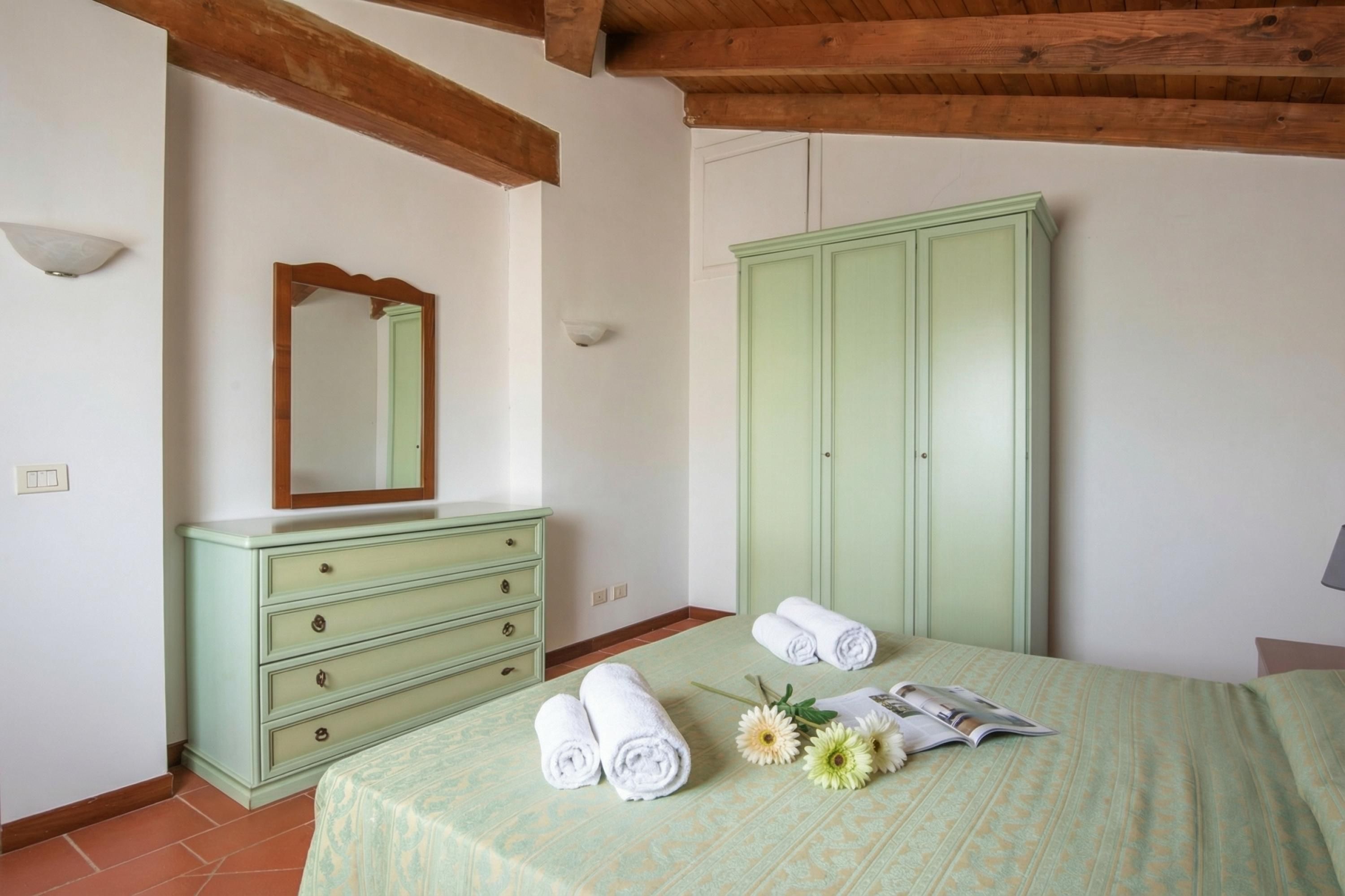 A bedroom with a bed, a green dresser, a mirror, and a wardrobe.